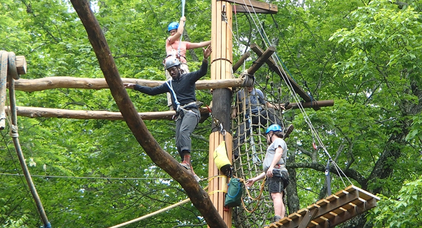 A group of people wearing safety gear navigate a high ropes course. 